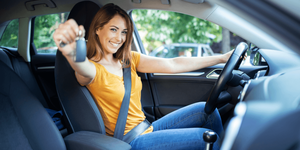 Lady sitting in the driver's seat, smiling and holding a car key, ready to drive.